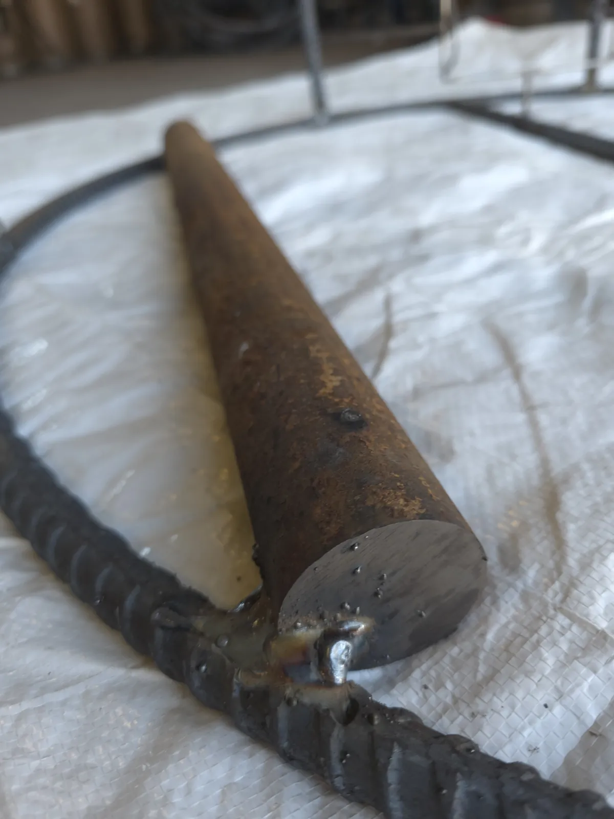 Close view of a round hot-roll weight bar welded to the bottom rebar ring of a bare CCP trap