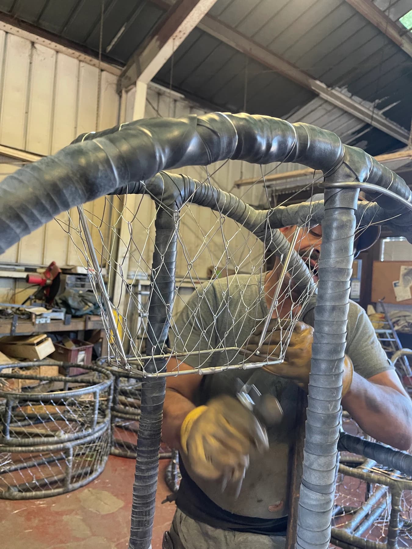A craftsperson hand-knitting wire mesh onto a crab pot frame in the shop
