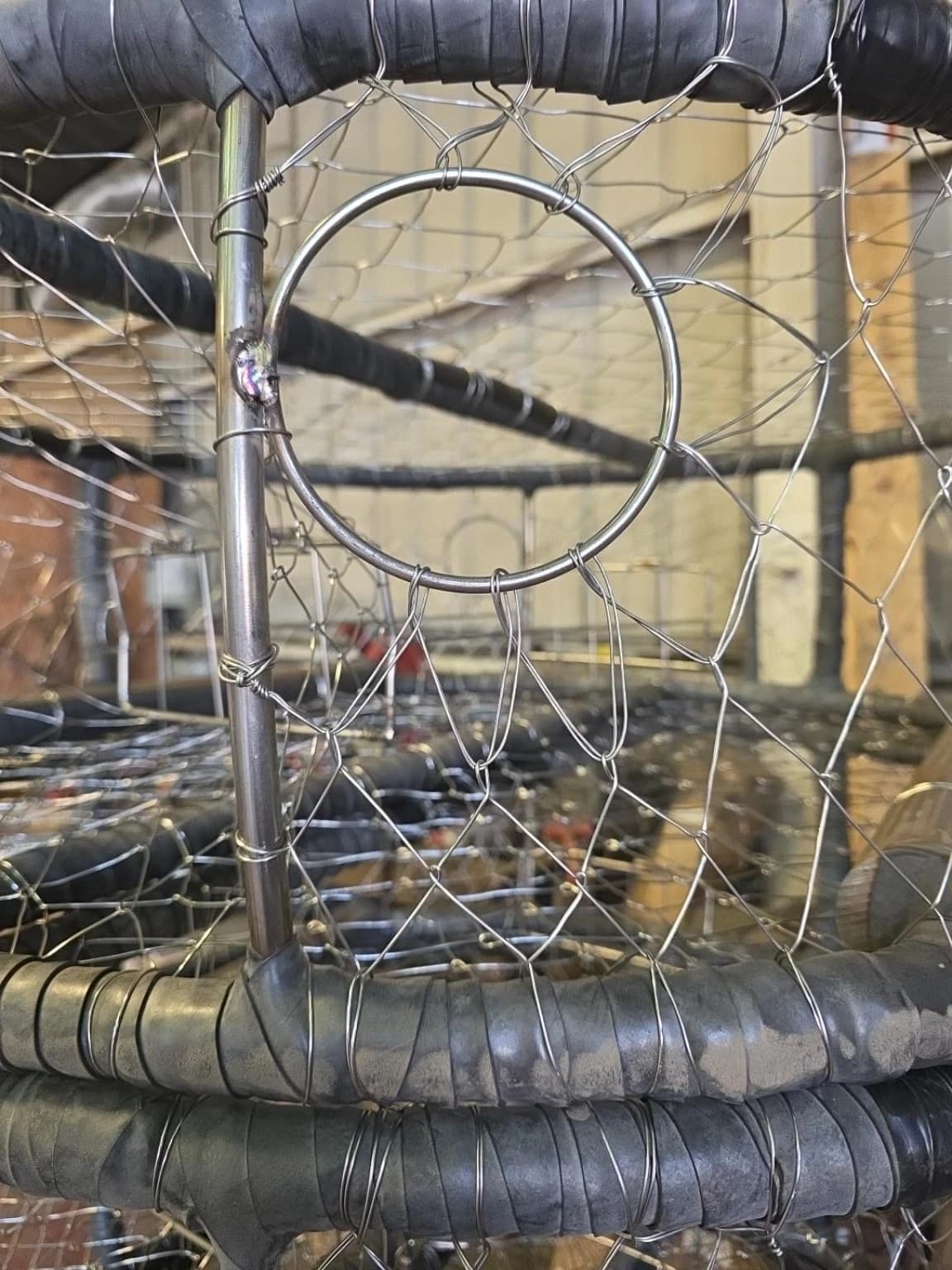 Close view of an escape ring welded to an unwrapped upright, with wire knitting around the ring