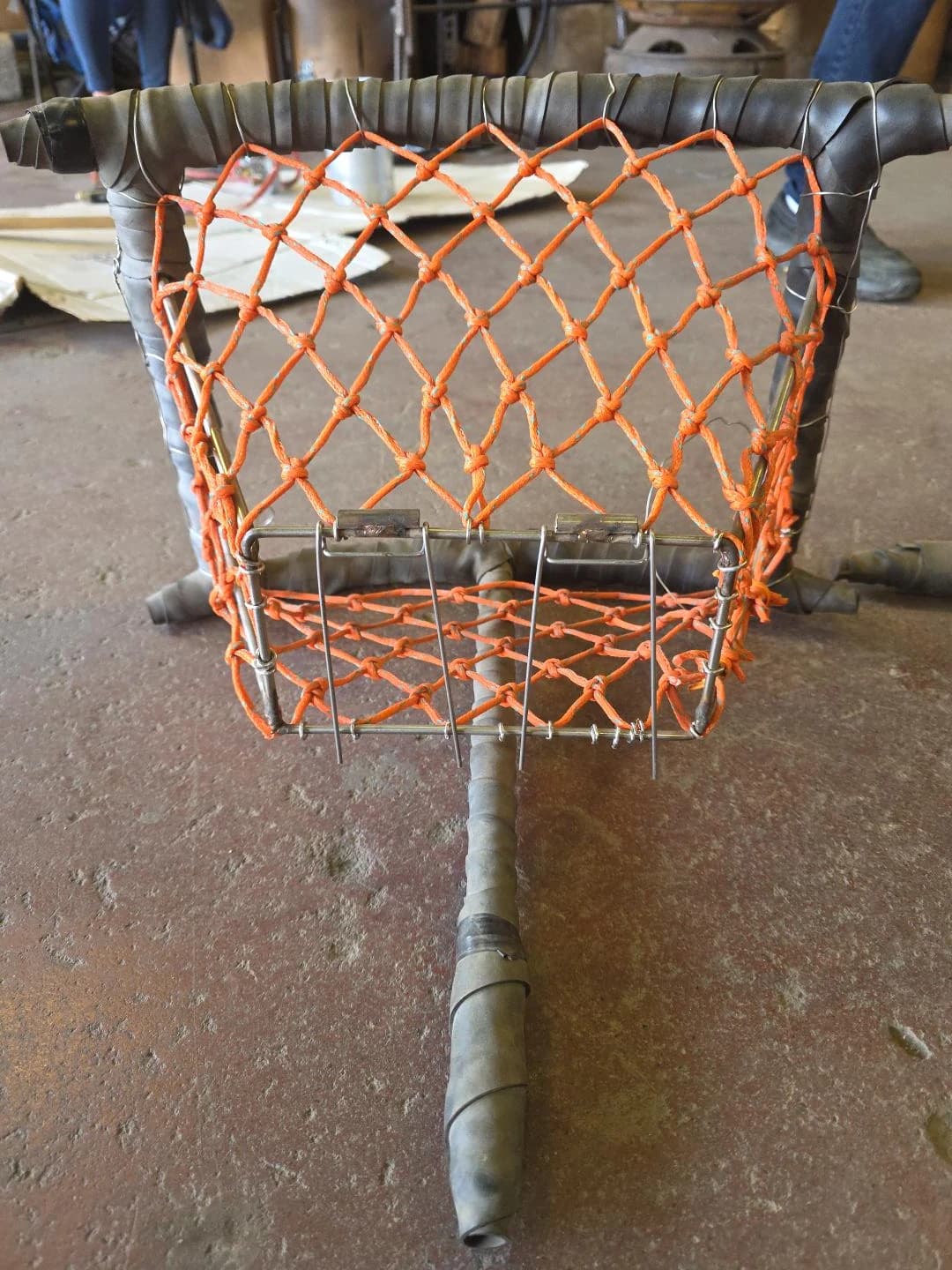 Front view of an orange braided tunnel showing the tapered mesh and rectangular trigger opening